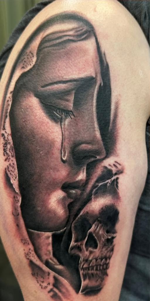 Black and gray veiled figure weeping above a skull, on a shoulder